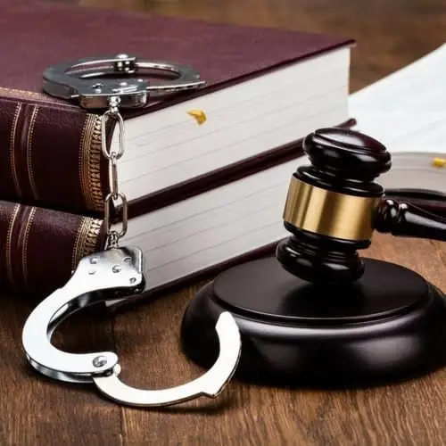 A judge’s gavel beside open handcuffs and law books on a wooden desk
